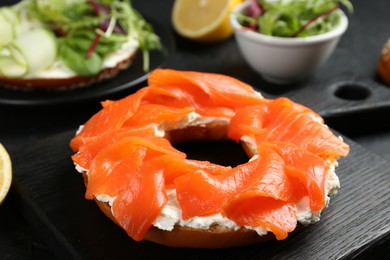 Photo of Delicious bagels with salmon and vegetables on black table, selective focus