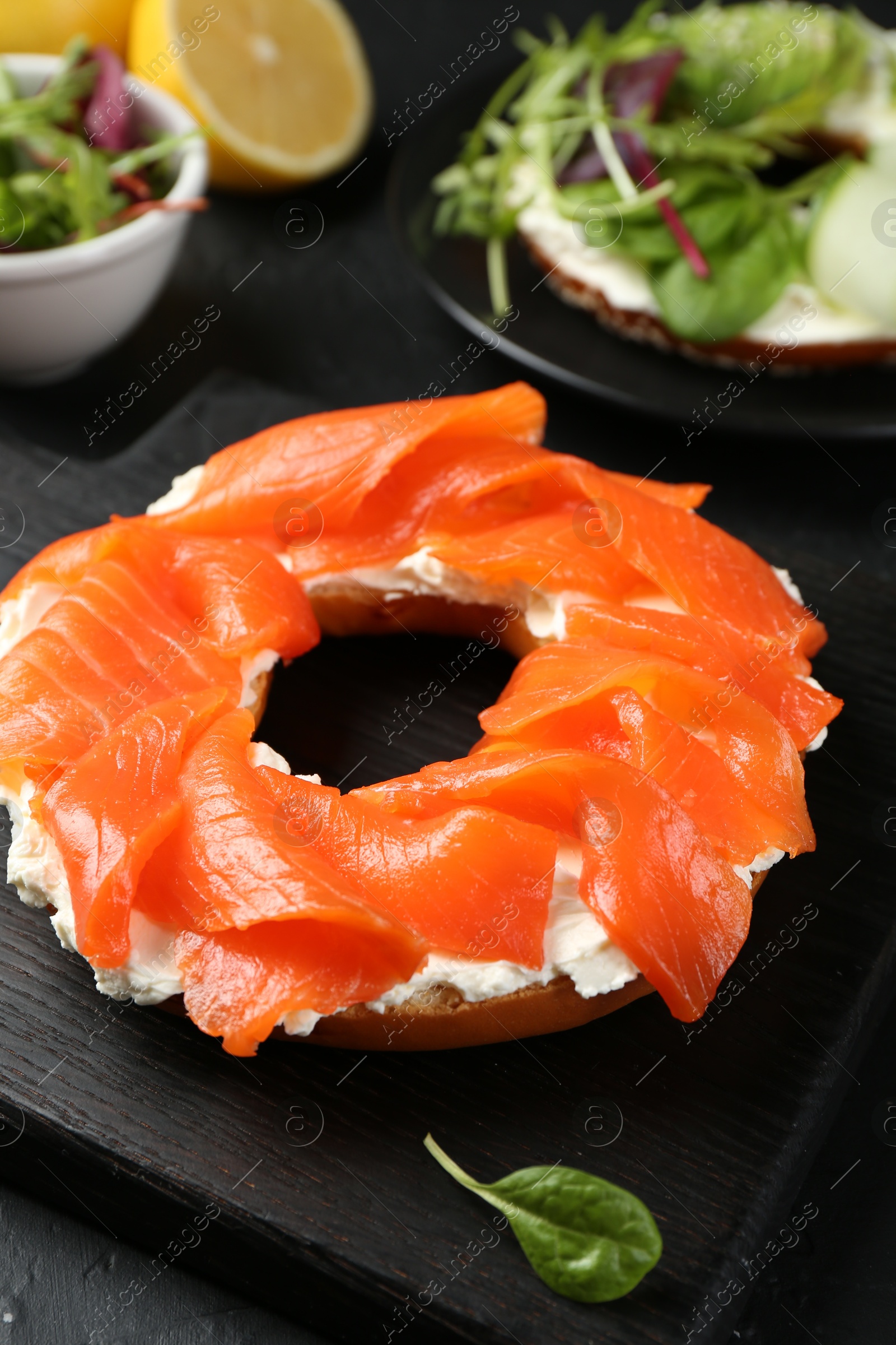 Photo of Delicious bagels with salmon and vegetables on black table, selective focus