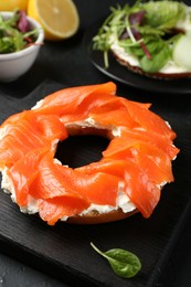 Photo of Delicious bagels with salmon and vegetables on black table, selective focus