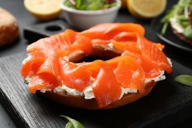 Photo of Delicious bagel with salmon and cream cheese n black table, closeup