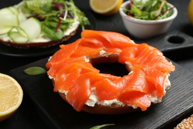 Photo of Delicious bagels with salmon and vegetables on black table, selective focus