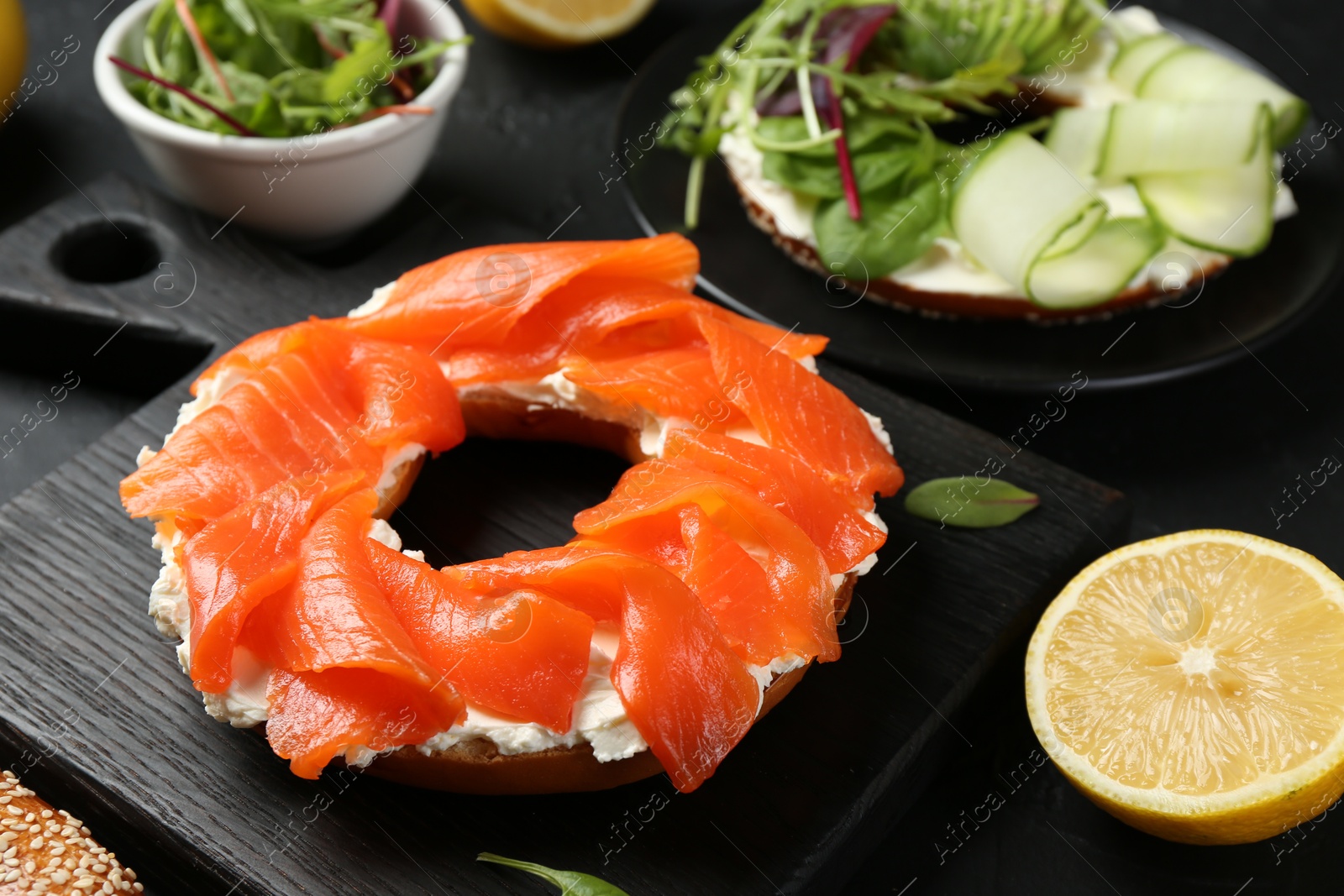 Photo of Delicious bagels with salmon and vegetables on black table, selective focus