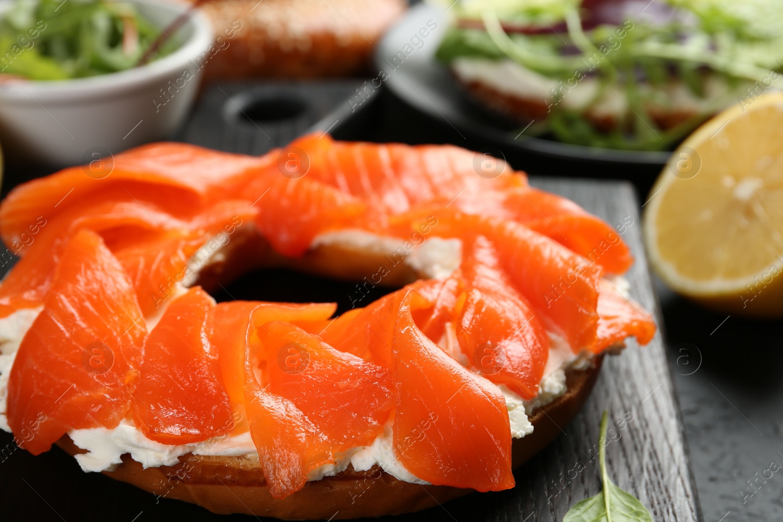 Photo of Delicious bagel with salmon and cream cheese n black table, closeup