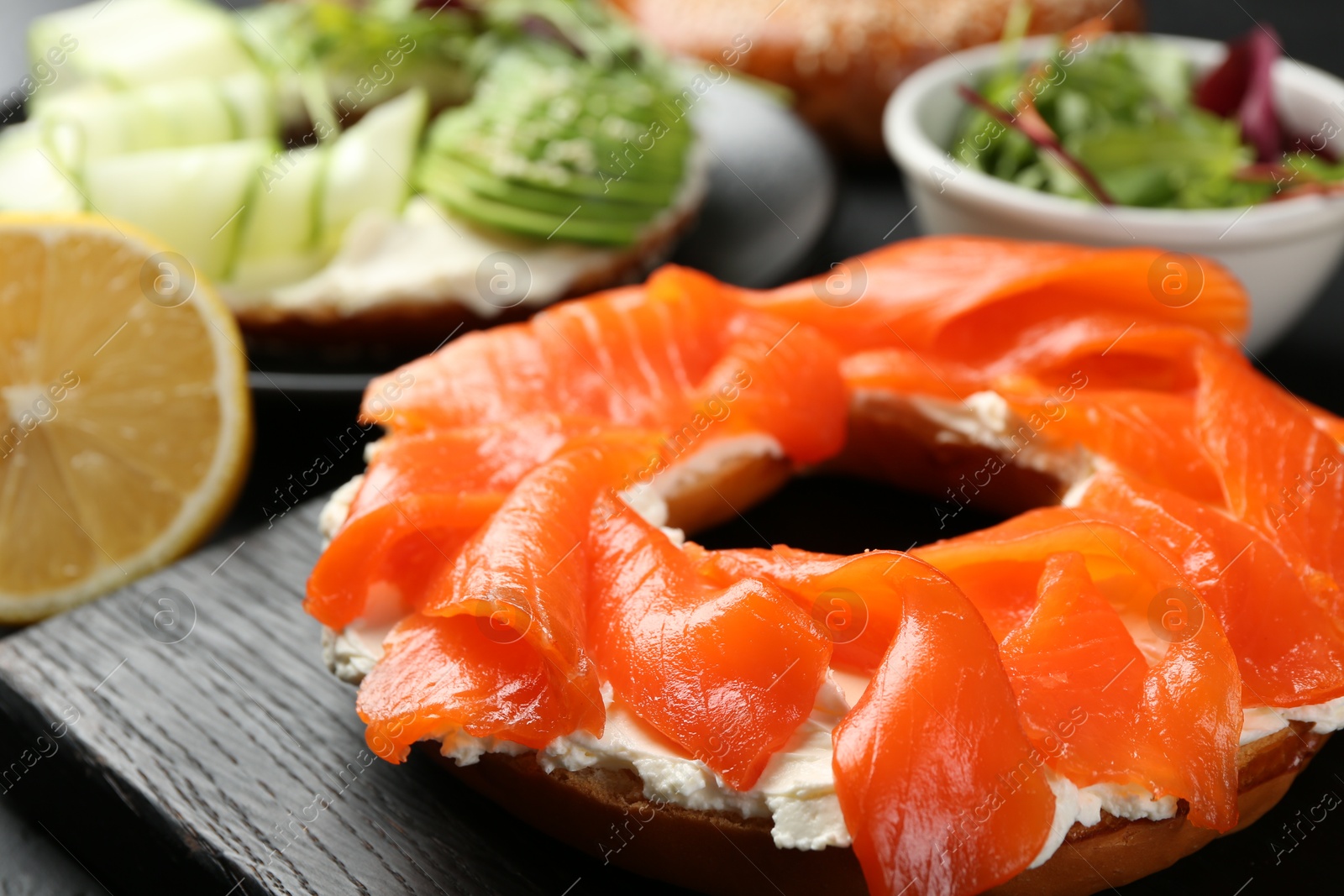 Photo of Delicious bagels with salmon and vegetables on black table, selective focus