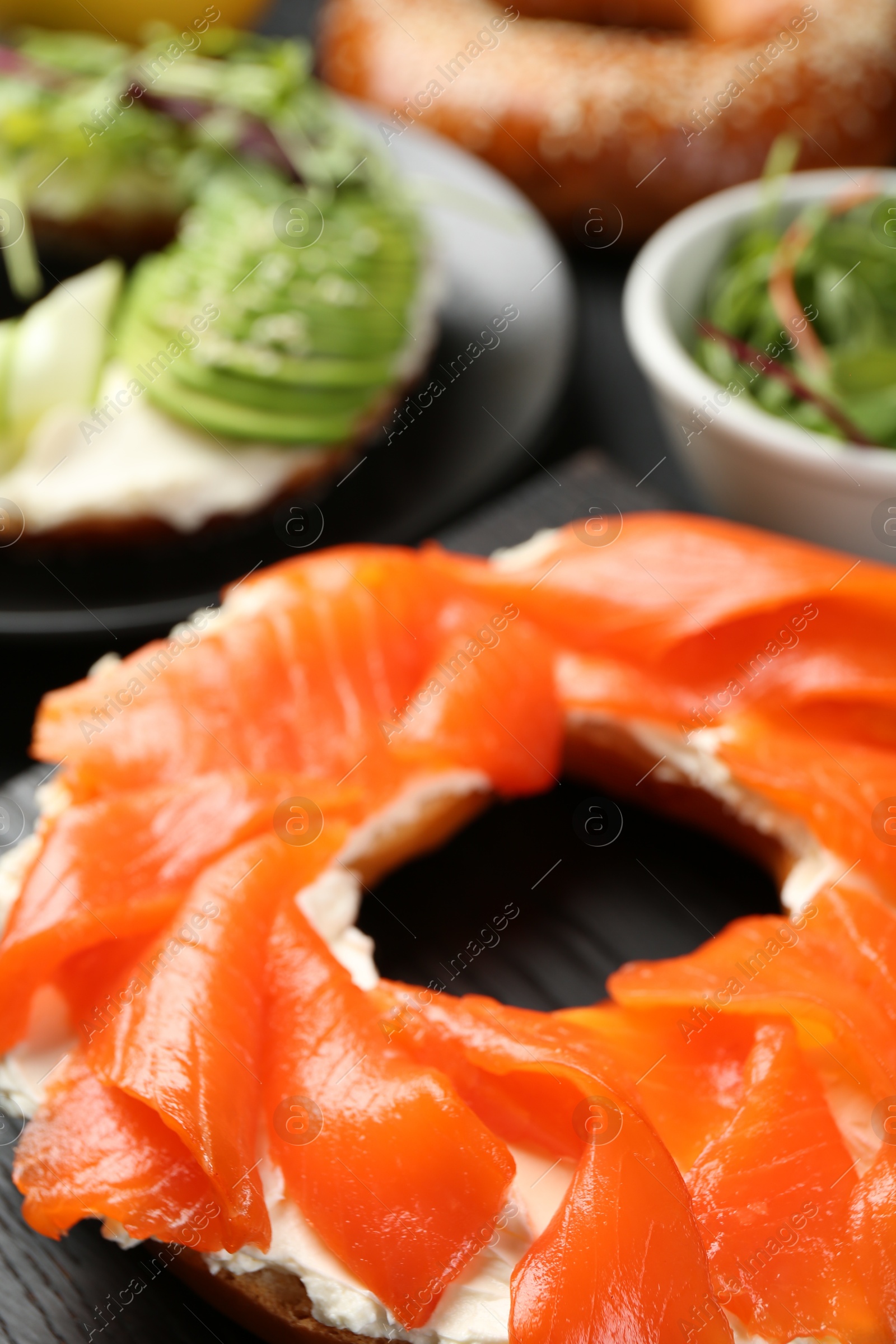 Photo of Delicious bagels with salmon and vegetables on black table, selective focus