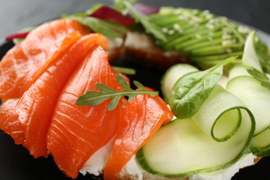 Photo of Delicious bagel with salmon, cream cheese, cucumber and avocado on black table, closeup