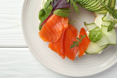 Photo of Delicious bagel with salmon, cream cheese, cucumber and avocado on white wooden table, top view