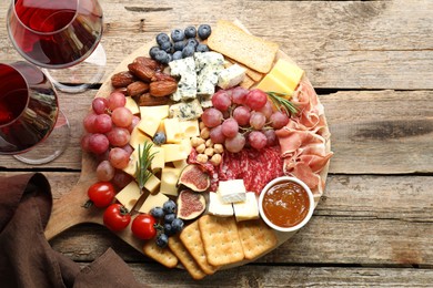 Photo of Different types of delicious cheese, other snacks and wine on wooden table, flat lay. Space for text