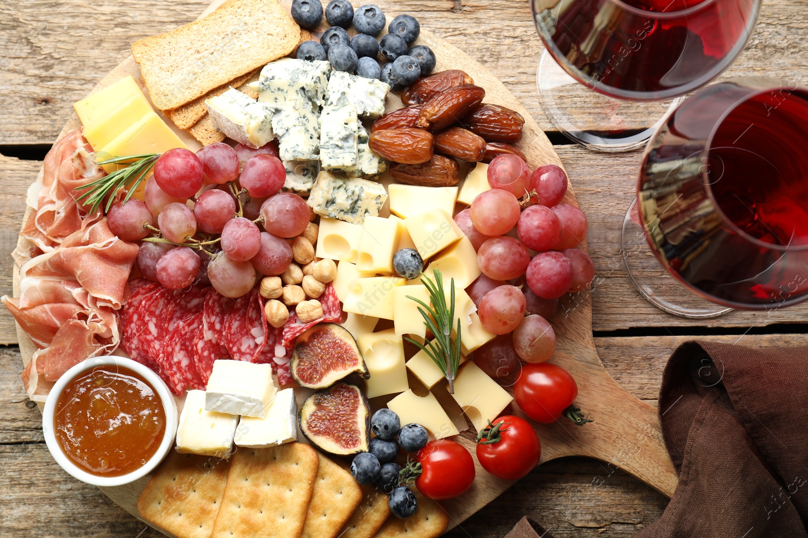 Photo of Different types of delicious cheese, other snacks and wine on wooden table, flat lay