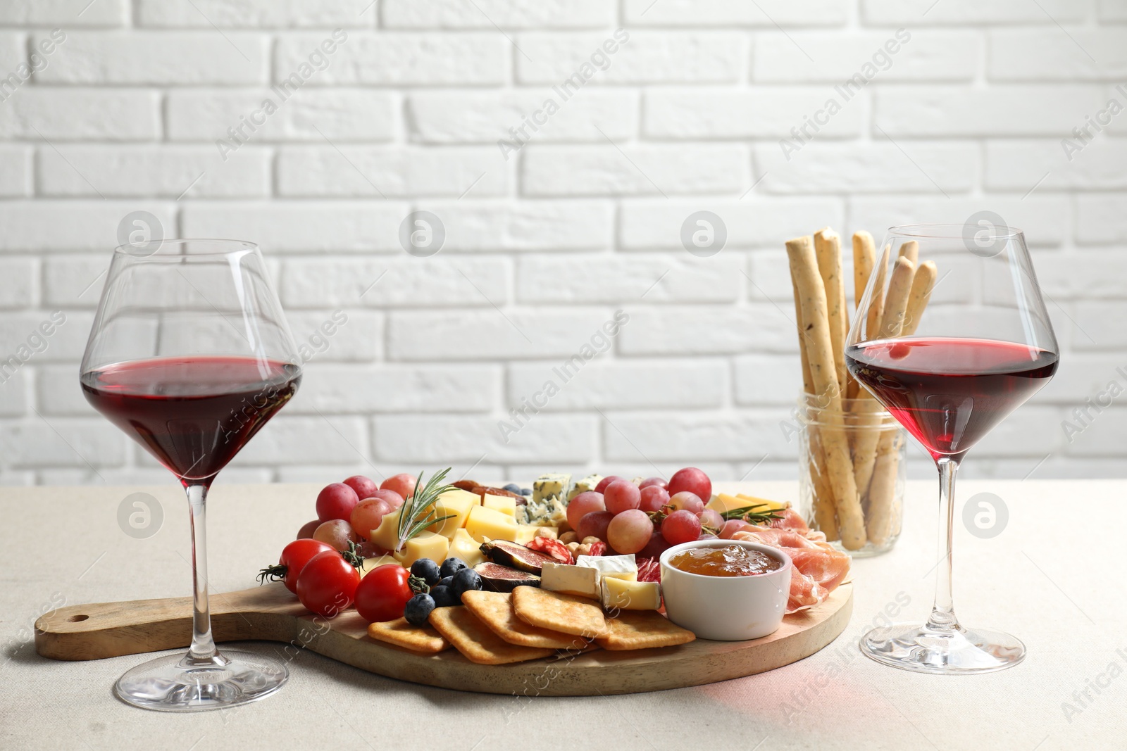 Photo of Different types of delicious cheese, other snacks and wine on light grey table