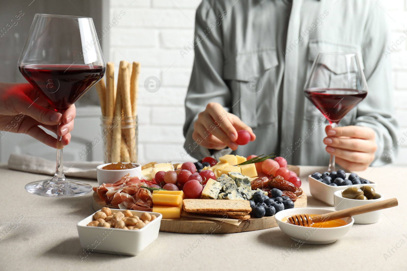 Photo of Women holding glasses of wine at light grey table with different snacks indoors, closeup