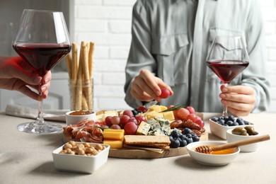 Photo of Women holding glasses of wine at light grey table with different snacks indoors, closeup