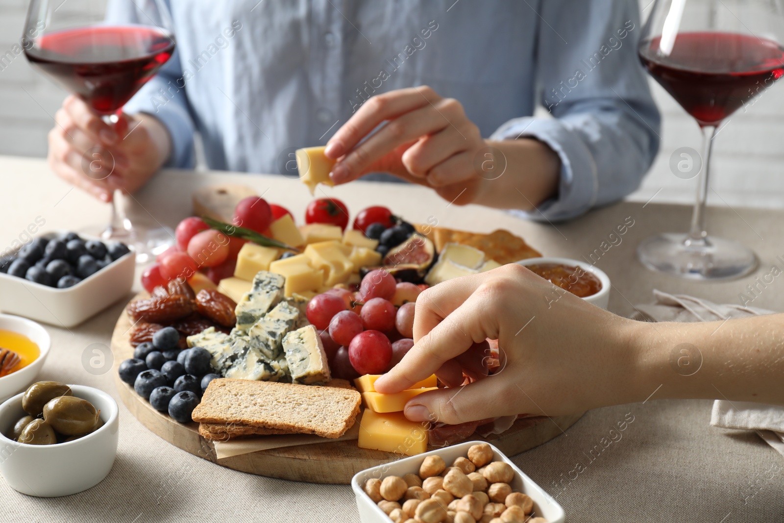 Photo of Women enjoying different snacks and wine during brunch at light grey table indoors, closeup