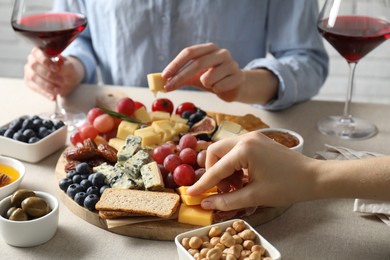 Photo of Women enjoying different snacks and wine during brunch at light grey table indoors, closeup