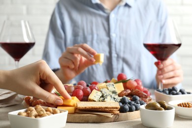 Photo of Women enjoying different snacks and wine during brunch at light grey table indoors, closeup