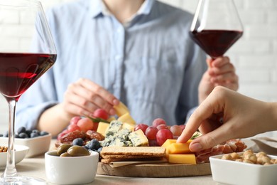 Photo of Women enjoying different snacks and wine during brunch at light grey table indoors, closeup