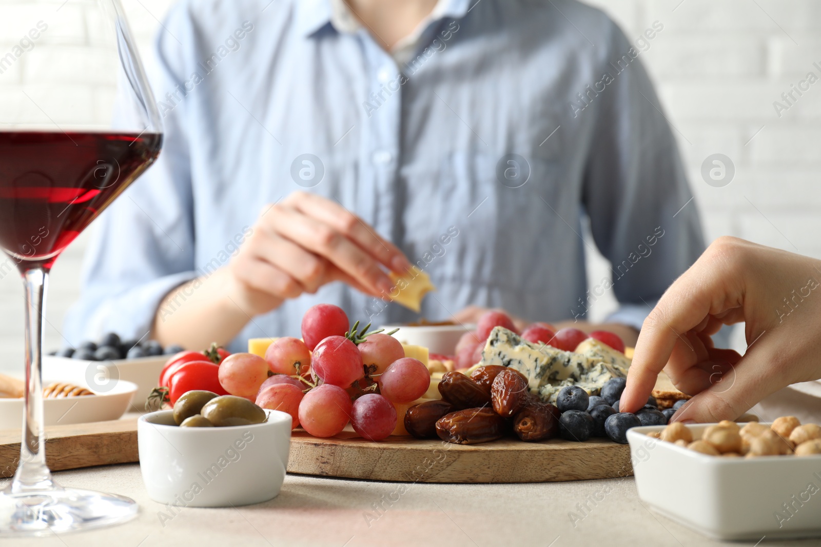 Photo of Women enjoying different snacks and wine during brunch at light grey table indoors, closeup