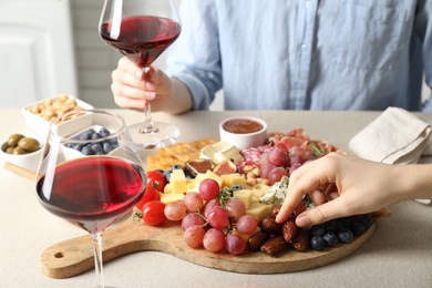 Photo of Women enjoying different snacks and wine during brunch at light grey table indoors, closeup