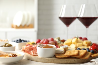 Photo of Different types of delicious cheese, other snacks and wine on light grey table, closeup