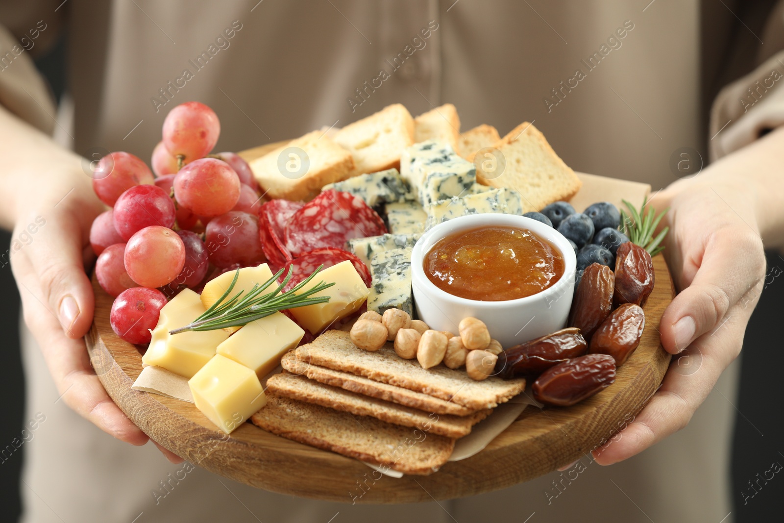 Photo of Woman holding board with different types of delicious cheese and other snacks, closeup