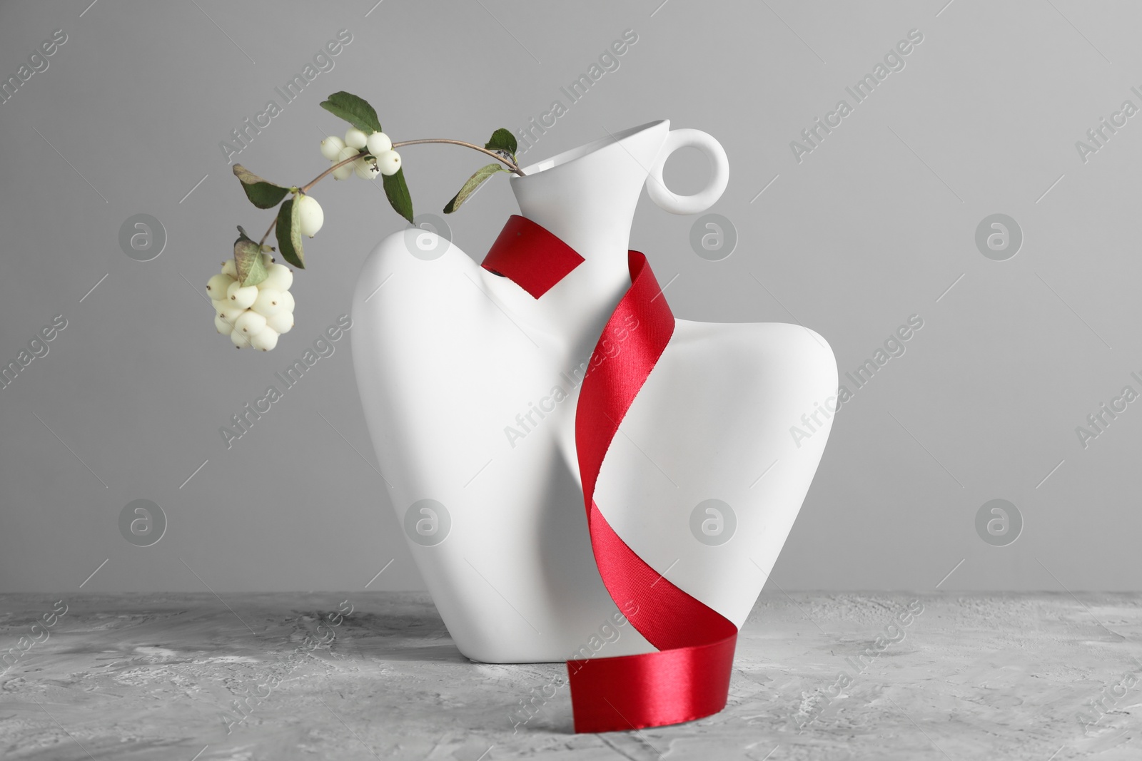 Photo of Stylish vase with snowberry branch and red ribbon on grey table