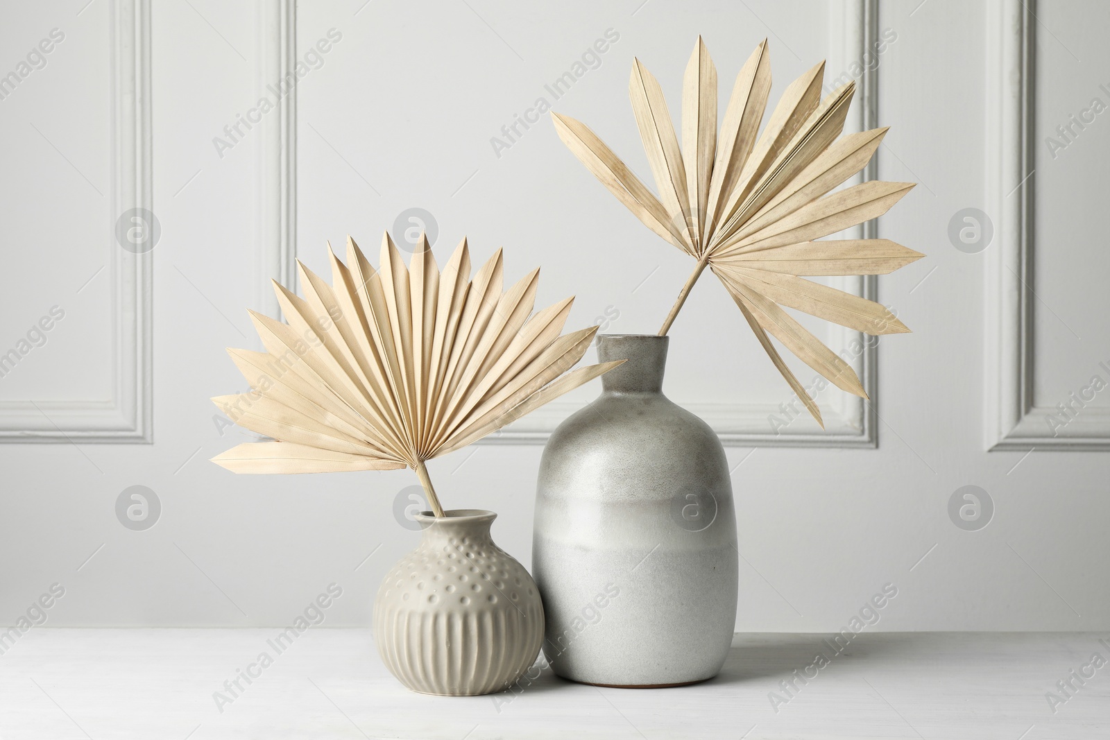 Photo of Stylish vases with dry palm leaves on white table