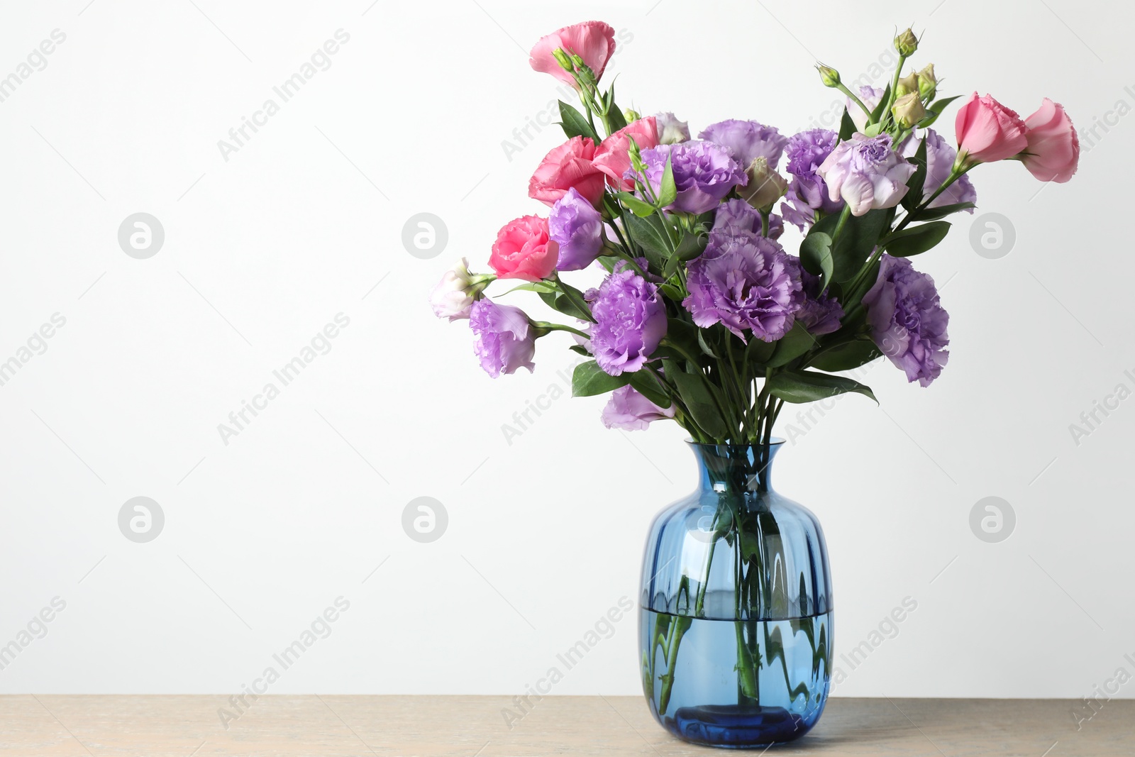 Photo of Vase with beautiful eustoma flowers on wooden table, space for text