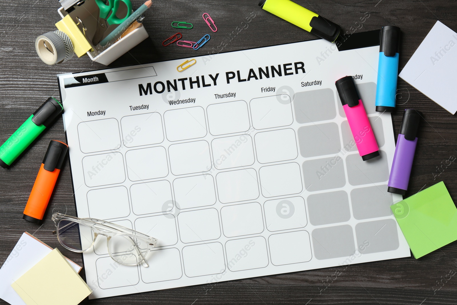 Photo of Timetable. Monthly planner and stationery on black wooden table, flat lay