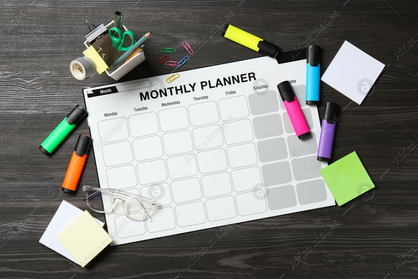 Photo of Timetable. Monthly planner and stationery on black wooden table, flat lay