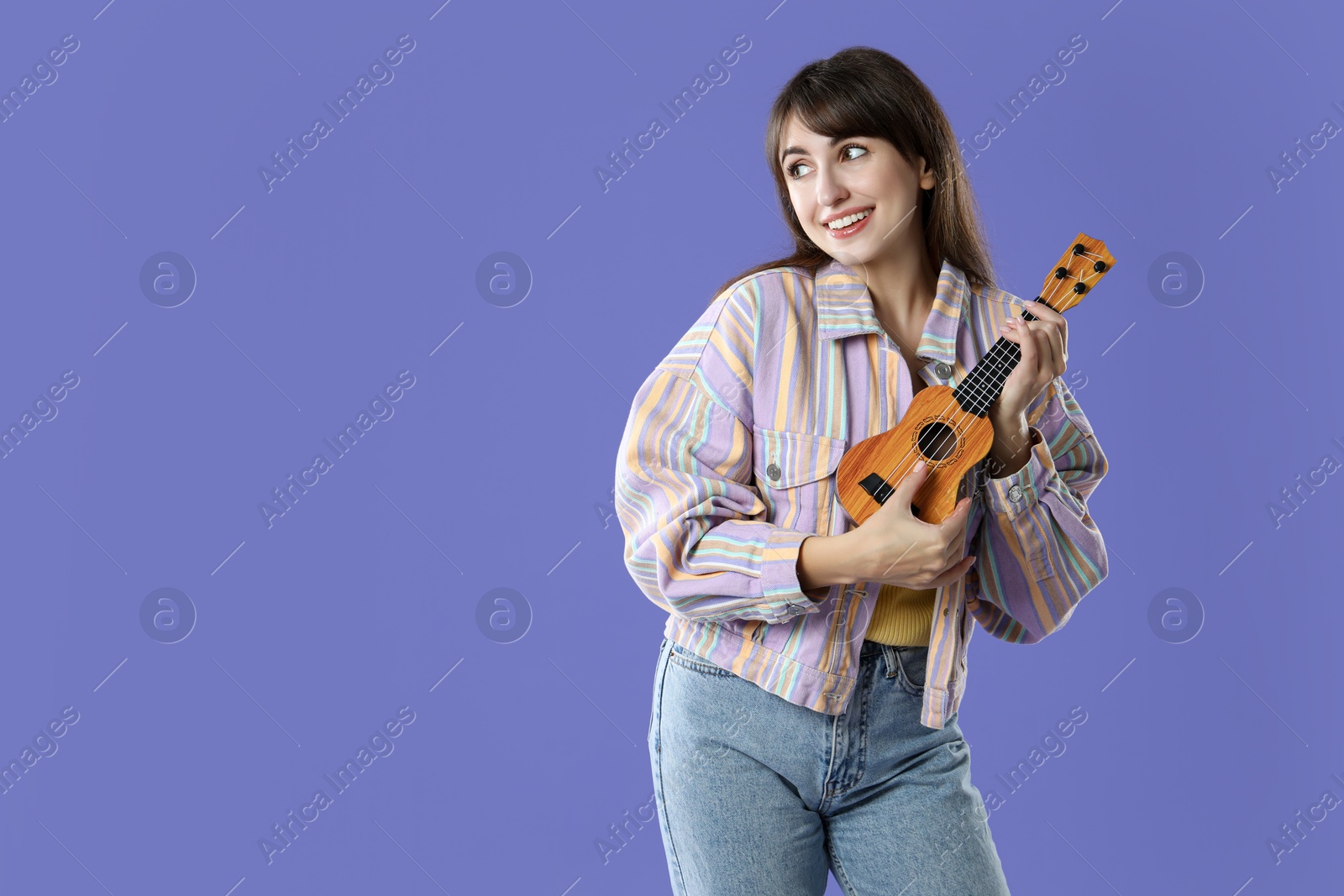 Photo of Happy woman playing ukulele on purple background, space for text