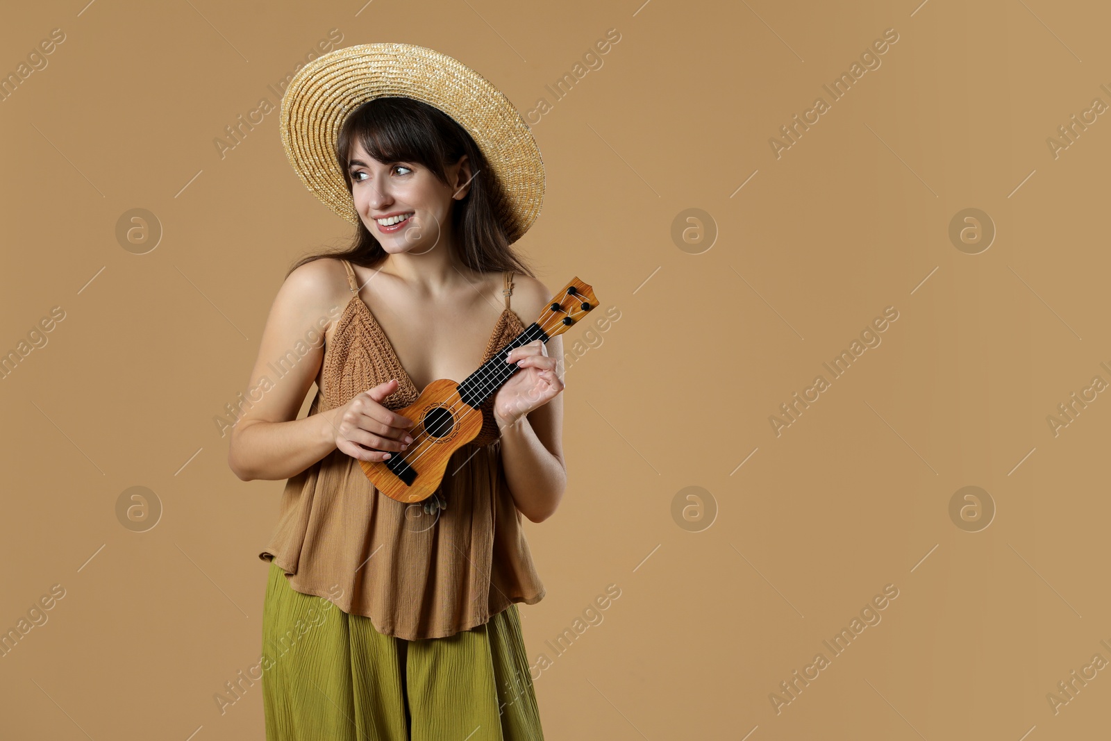 Photo of Happy woman playing ukulele on beige background, space for text