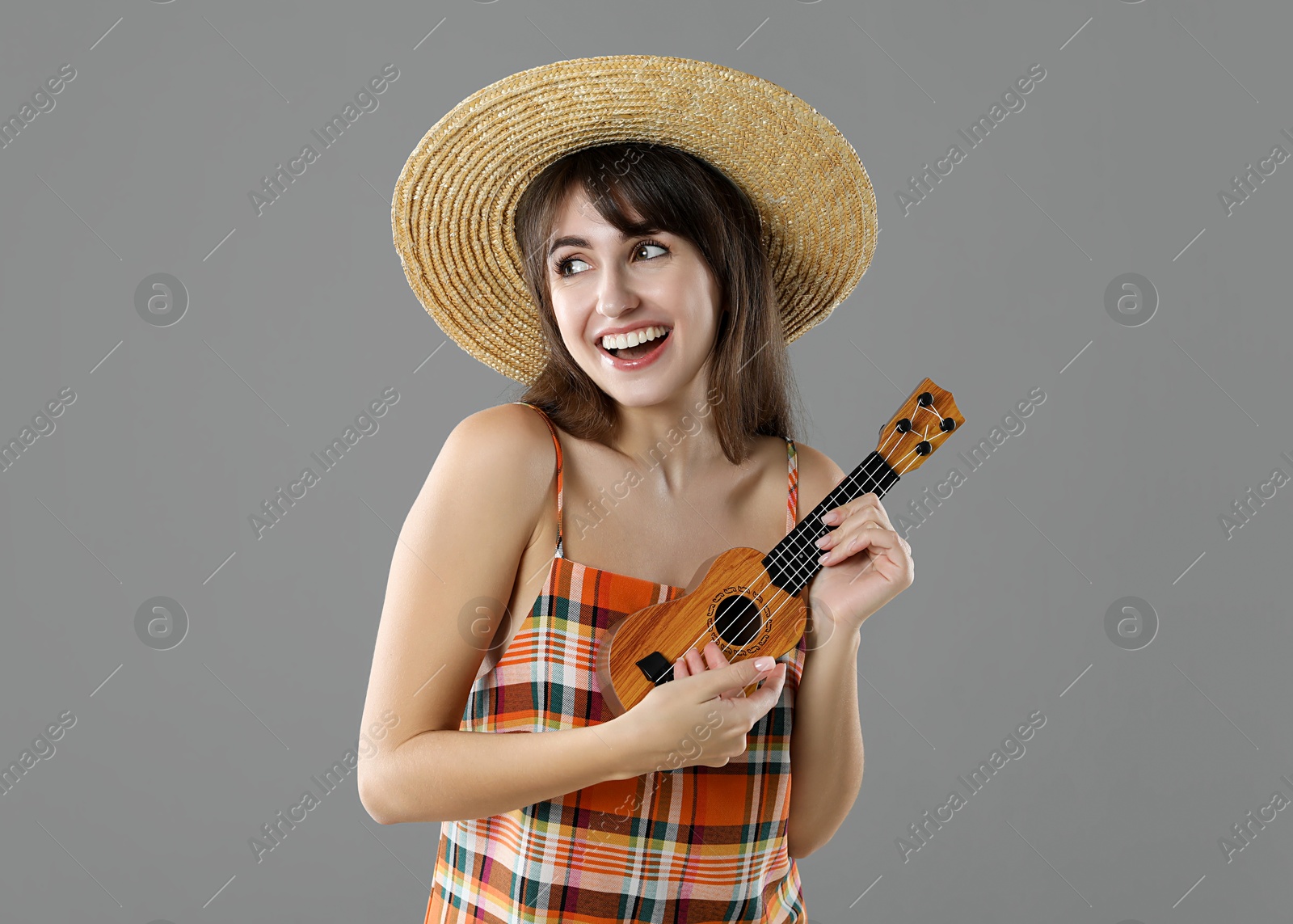 Photo of Happy woman playing ukulele on grey background