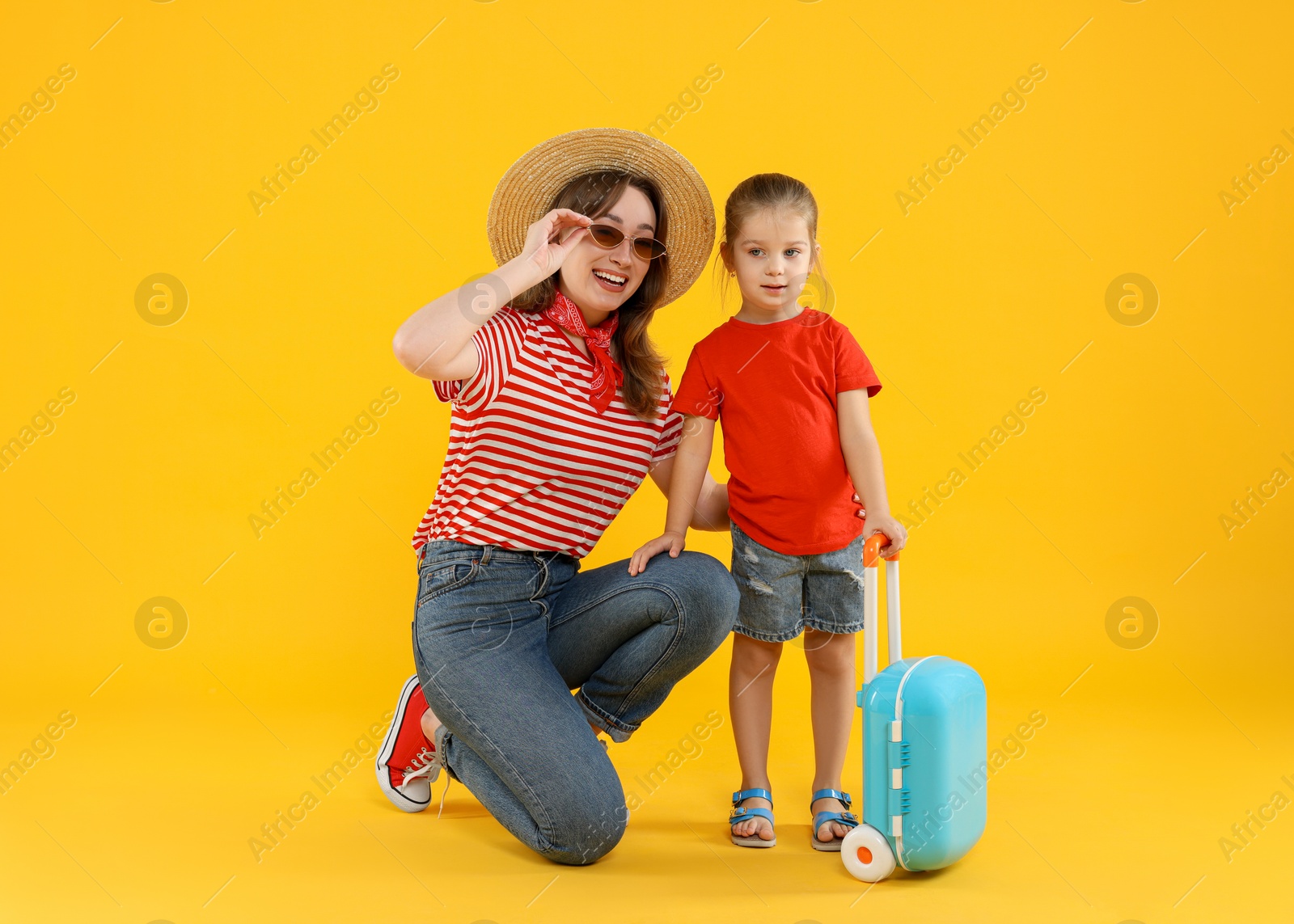 Photo of Traveller with suitcase. Young woman and cute little girl on yellow background