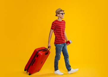 Photo of Happy traveller with suitcase, passport and ticket on yellow background