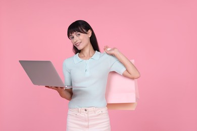 Photo of Internet shopping. Happy woman with laptop and colorful bags on pink background