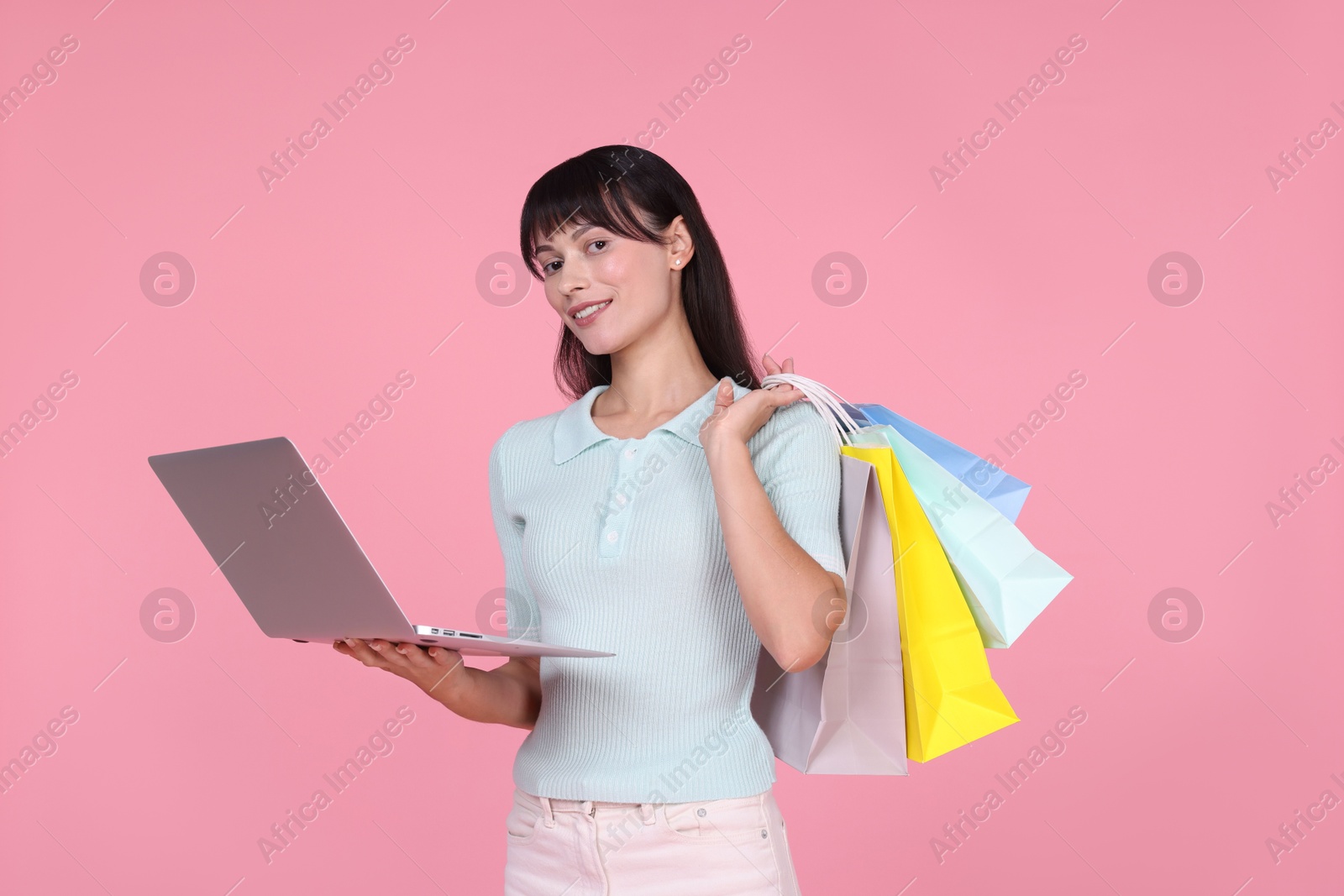 Photo of Internet shopping. Happy woman with laptop and colorful bags on pink background