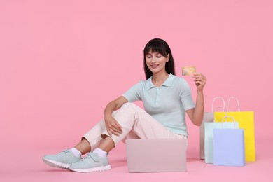 Photo of Internet shopping. Happy woman with credit card, laptop and colorful bags on pink background