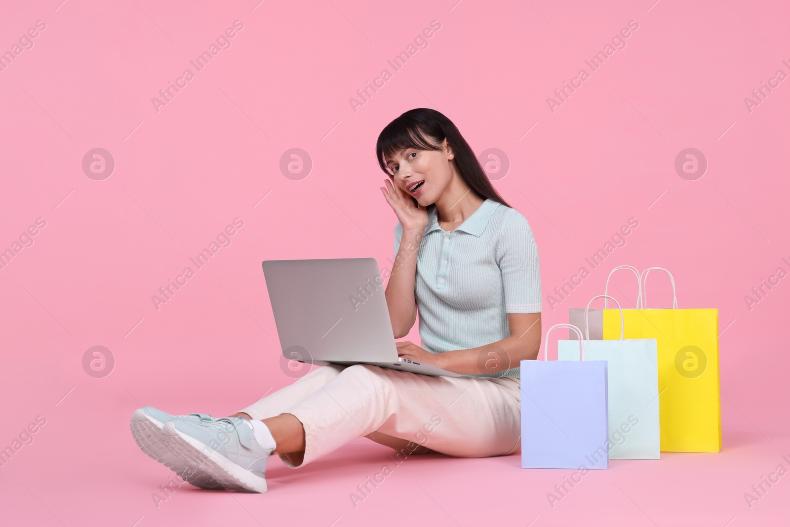 Photo of Internet shopping. Happy woman with laptop and colorful bags on pink background