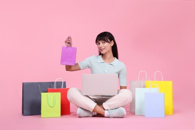 Photo of Internet shopping. Happy woman with laptop and colorful bags on pink background