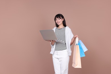 Photo of Internet shopping. Happy woman with laptop and colorful bags on beige background, space for text