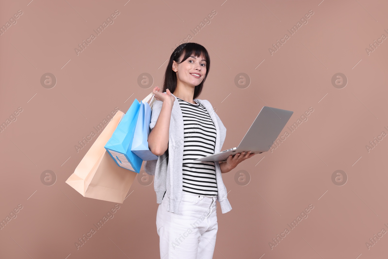 Photo of Internet shopping. Happy woman with laptop and colorful bags on beige background