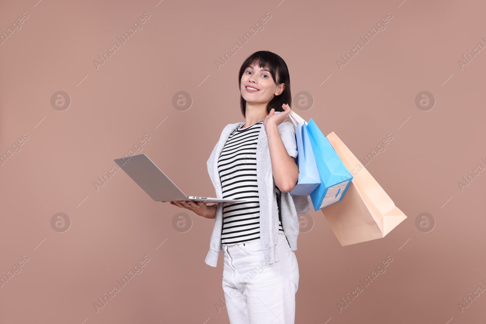 Photo of Internet shopping. Happy woman with laptop and colorful bags on beige background