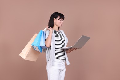 Photo of Internet shopping. Happy woman with laptop and colorful bags on beige background