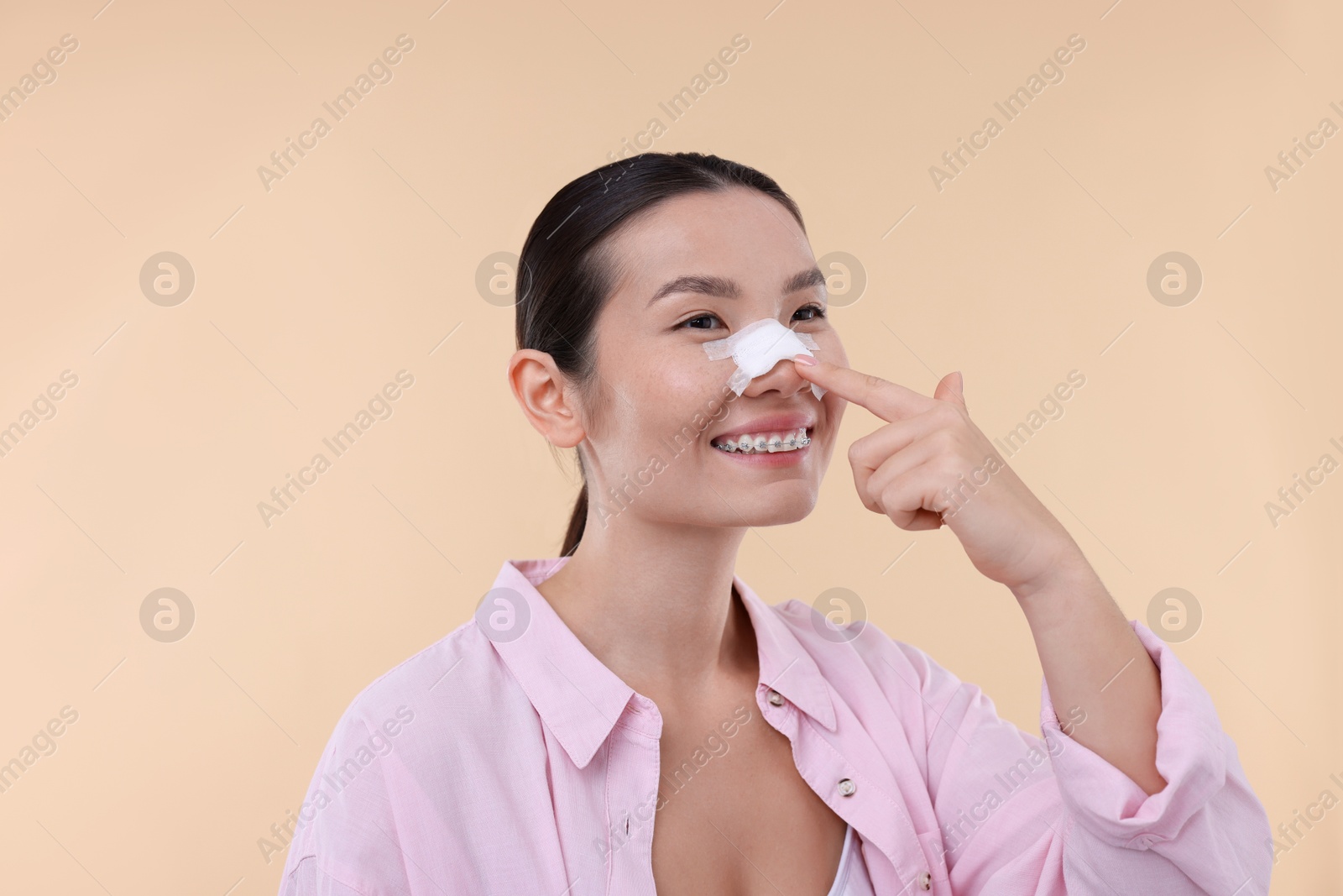 Photo of Woman with medical bandage on her nose after plastic surgery operation against beige background