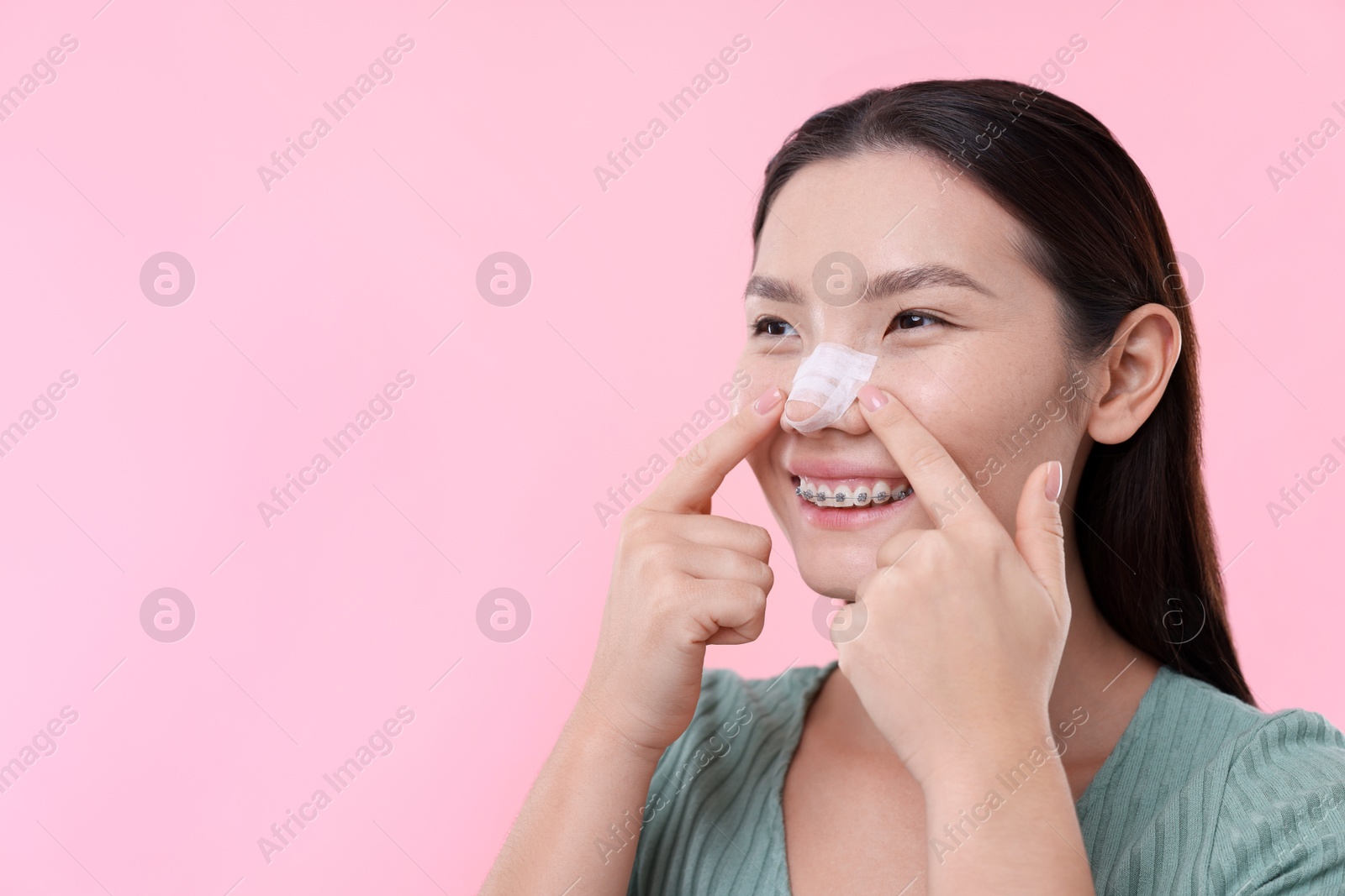 Photo of Woman with medical bandage on her nose after plastic surgery operation against pink background. Space for text