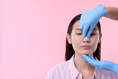 Photo of Doctor checking patient's nose after plastic surgery operation on pink background, closeup. Space for text