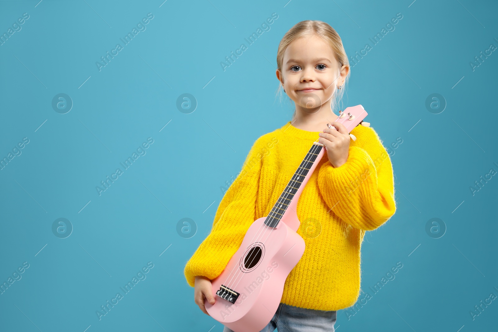 Photo of Little girl with ukulele on light blue background, space for text