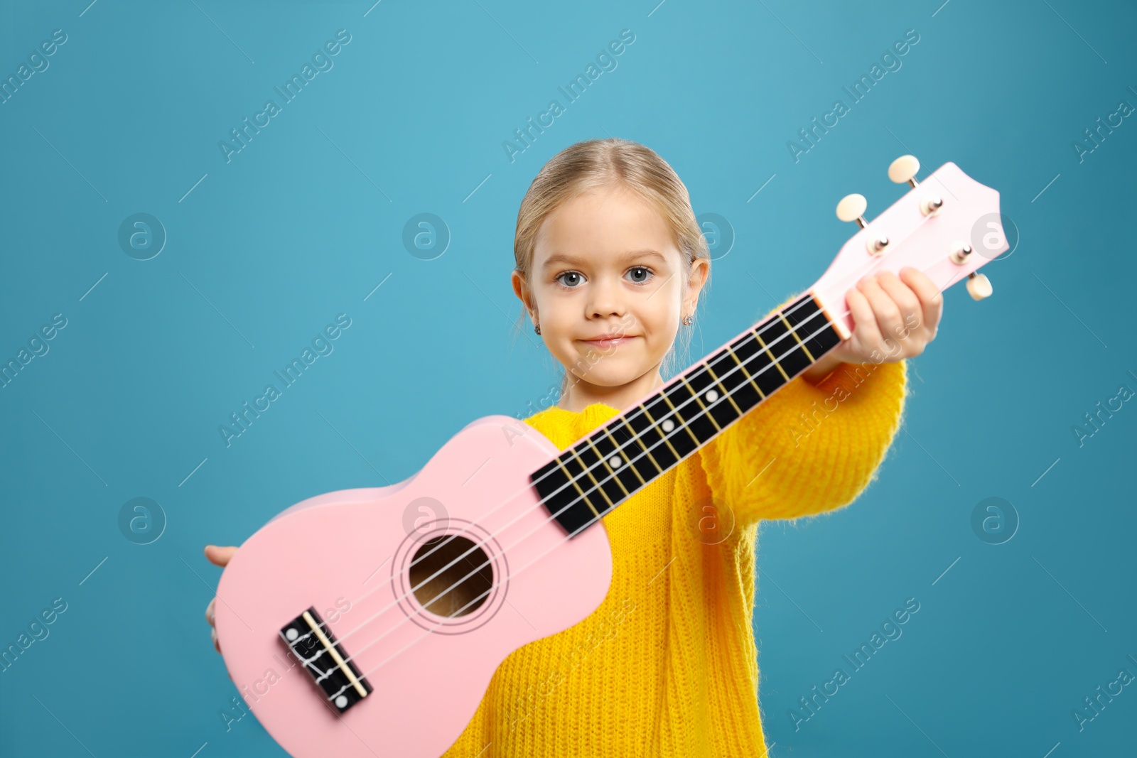 Photo of Little girl with ukulele on light blue background