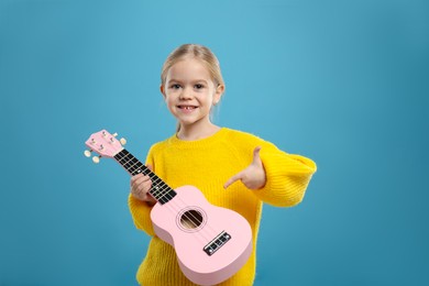 Photo of Little girl with ukulele on light blue background