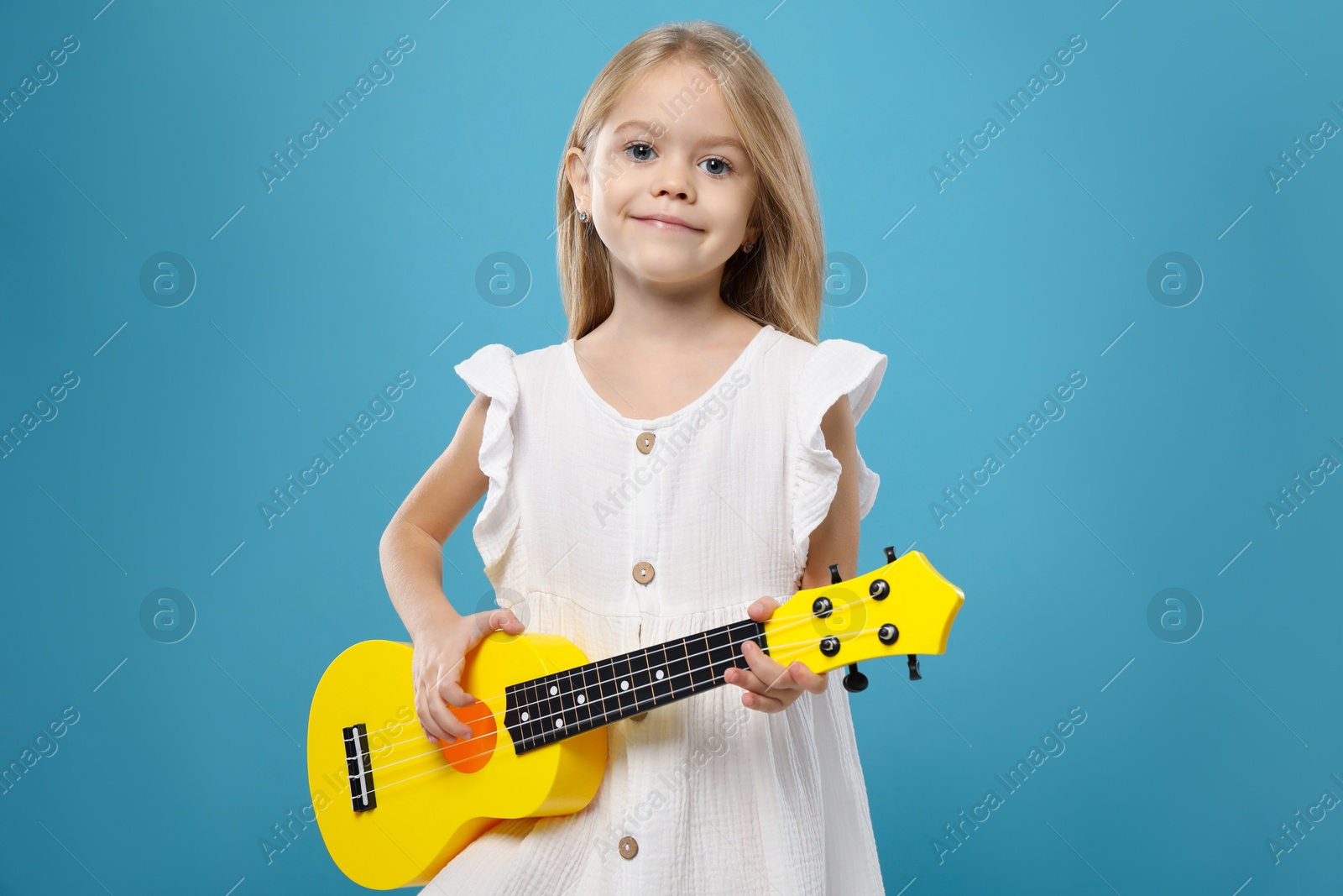 Photo of Little girl playing ukulele on light blue background